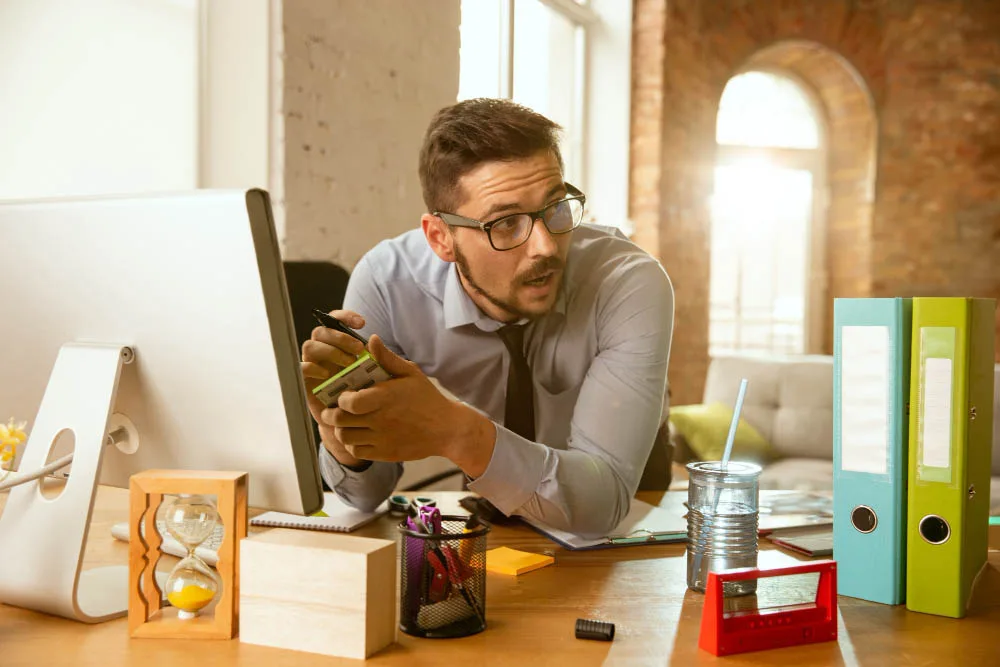 A young man sits at a desk in an office, focused on his monitor, embodying the role of a Product Owner in Agile development. The workspace is equipped with modern office essentials.